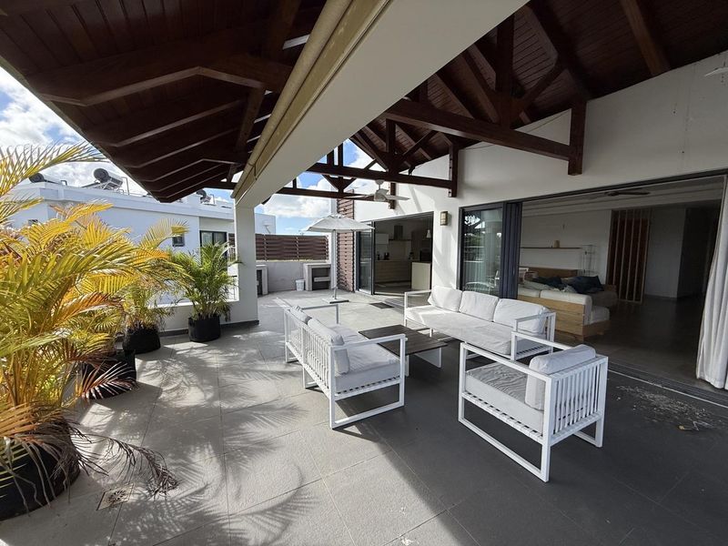 Spacious covered penthouse balcony featuring exposed timber beams, tiled flooring, and seamless indoor-outdoor flow through large sliding glass doors.