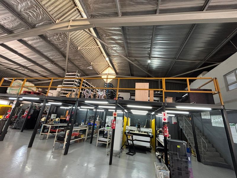 Spacious industrial warehouse featuring a mezzanine level, steel staircase, high-clearance exposed roof structure, and durable epoxy flooring suitable for manufacturing or storage operations.
