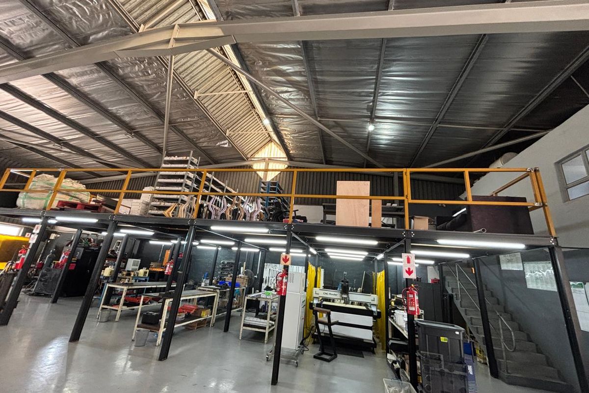 Spacious industrial warehouse featuring a mezzanine level, steel staircase, high-clearance exposed roof structure, and durable epoxy flooring suitable for manufacturing or storage operations.