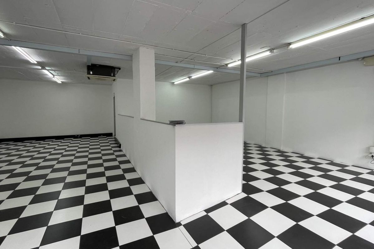 An open-plan retail space featuring checkered flooring, built-in partition wall, and functional overhead lighting, suitable for various commercial business layouts.