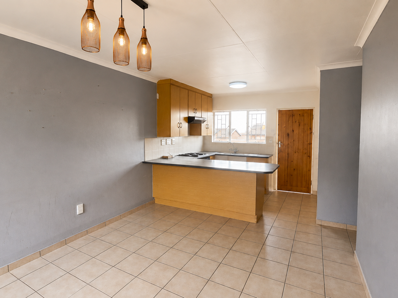 Open-plan kitchen and living area featuring tiled flooring, built-in wooden cabinetry, and direct access to an exterior door.