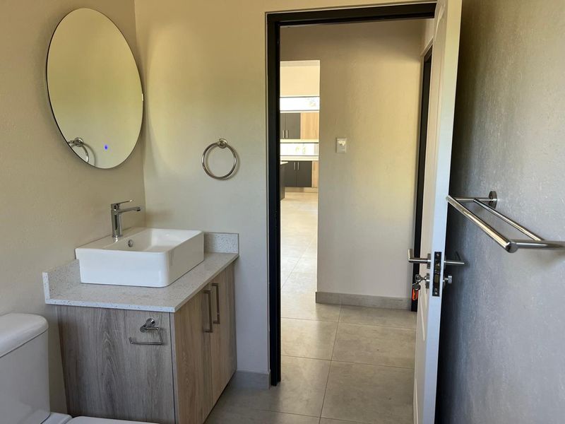 A modern, clean bathroom featuring a vessel sink on a wood-finish vanity, a round mirror, and neutral floor tiles.