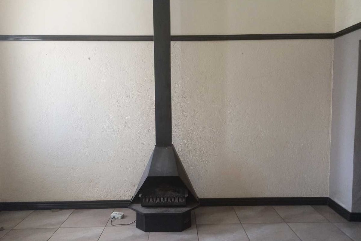 A living room featuring a central freestanding metal fireplace, tiled flooring, and dark wood-style trim detailing.