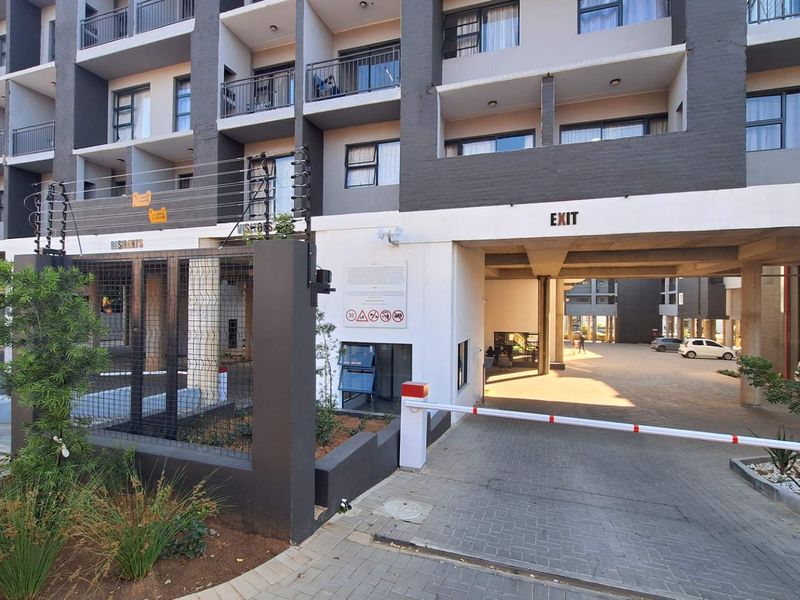 Exterior view of a modern apartment complex featuring a secure gated entrance, paved driveway, and multi-level balconies.