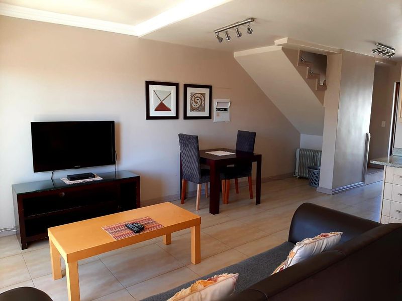 Open-plan living and dining area featuring tiled flooring, a staircase, and modern lighting fixtures, providing a functional and connected layout.