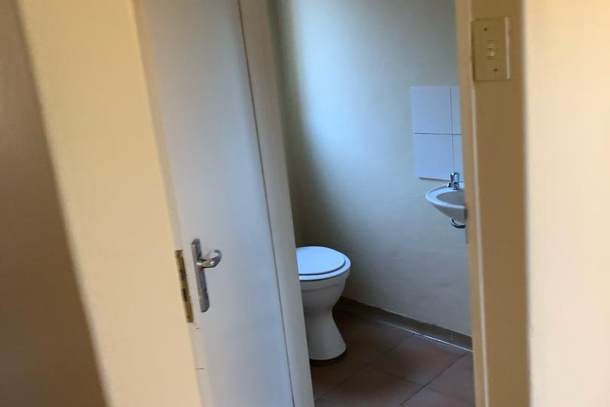 A small, functional guest bathroom featuring a toilet and a wall-mounted basin with tiled flooring.