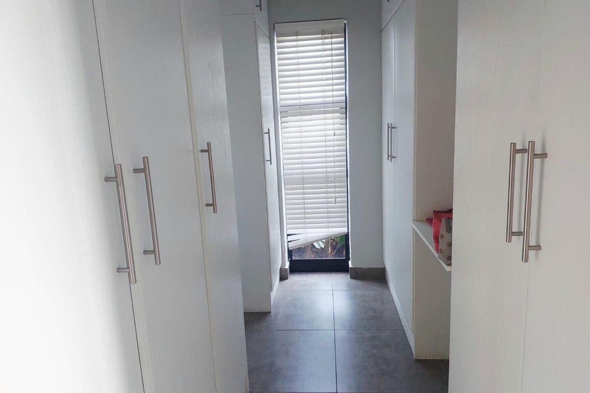 A walk-in closet or dressing area featuring floor-to-ceiling built-in white cabinetry, tiled flooring, and a window with fitted blinds.