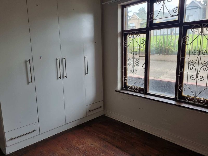 A vacant bedroom featuring built-in cupboards, timber flooring, and a window fitted with security bars.