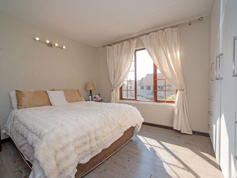 A well-lit bedroom featuring laminate flooring, built-in cupboards, and timber-framed windows, offering a comfortable and functional living space.
