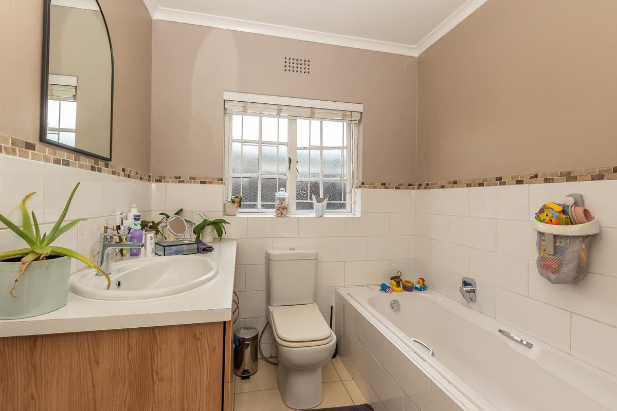 A functional bathroom featuring a built-in vanity with basin, a standard bathtub, and a toilet, finished with neutral wall tiles and a mosaic border.