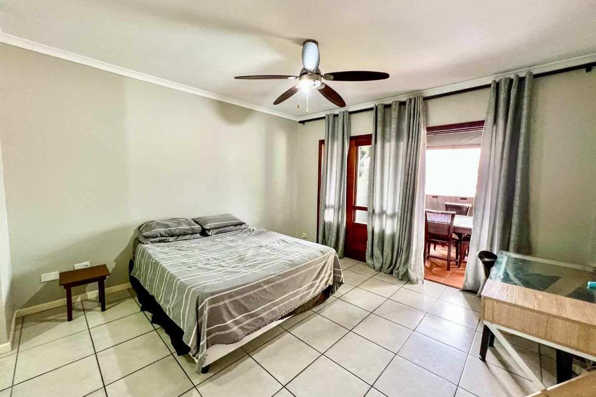 Spacious bedroom featuring tiled flooring, a ceiling fan, and direct access to an outdoor patio area through glass-paned doors.