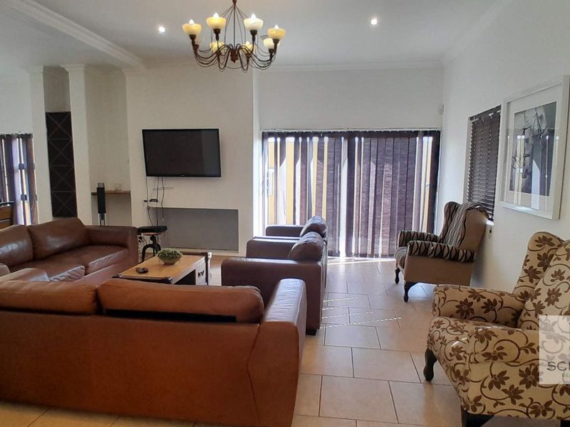 Spacious living room featuring tiled flooring, recessed downlighting, a decorative chandelier, and large windows with fitted blinds.