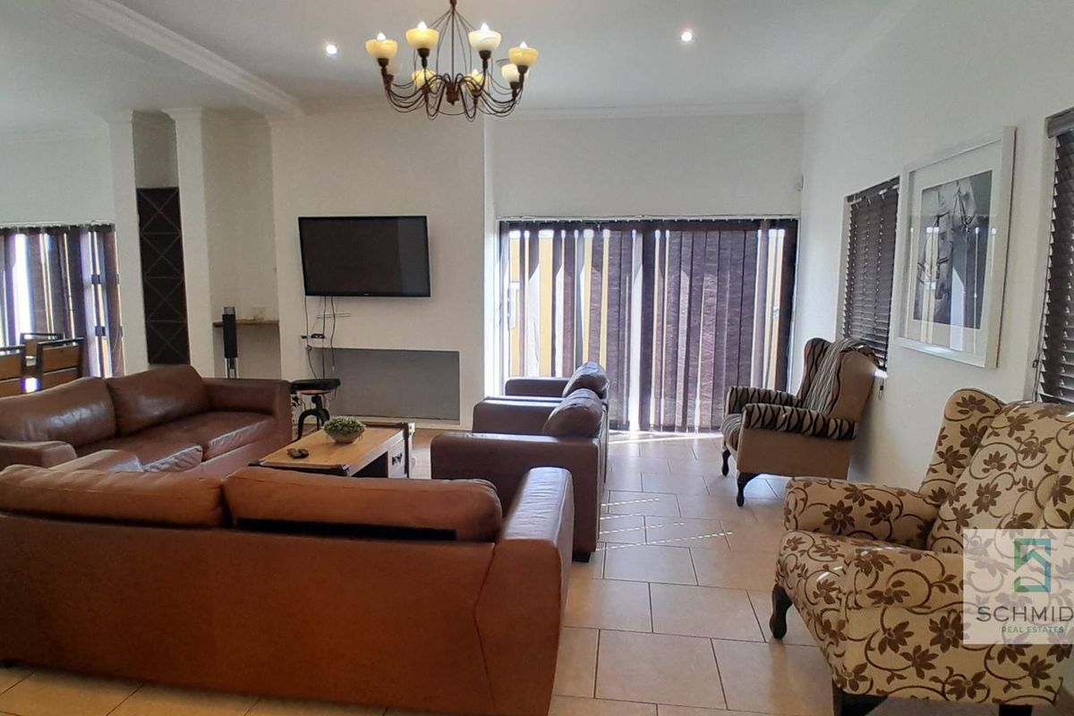 Spacious living room featuring tiled flooring, recessed downlighting, a decorative chandelier, and large windows with fitted blinds.