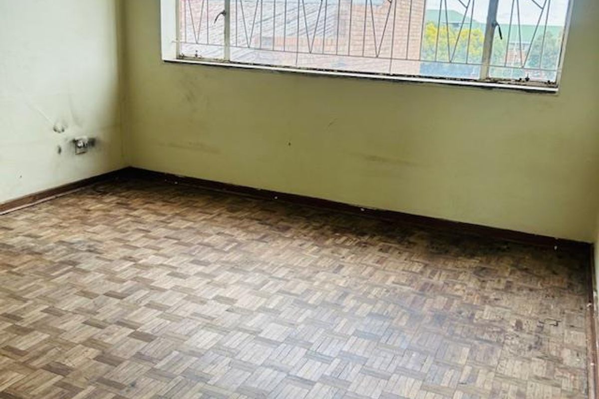 An empty bedroom featuring original parquet flooring and a large window fitted with security bars.