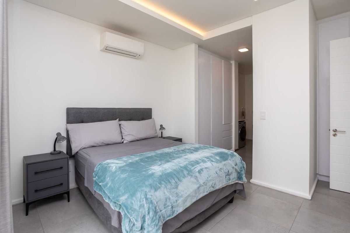 A modern, well-maintained bedroom featuring built-in cupboards, recessed ceiling lighting, and an integrated air conditioning unit, with neutral tiled flooring throughout.