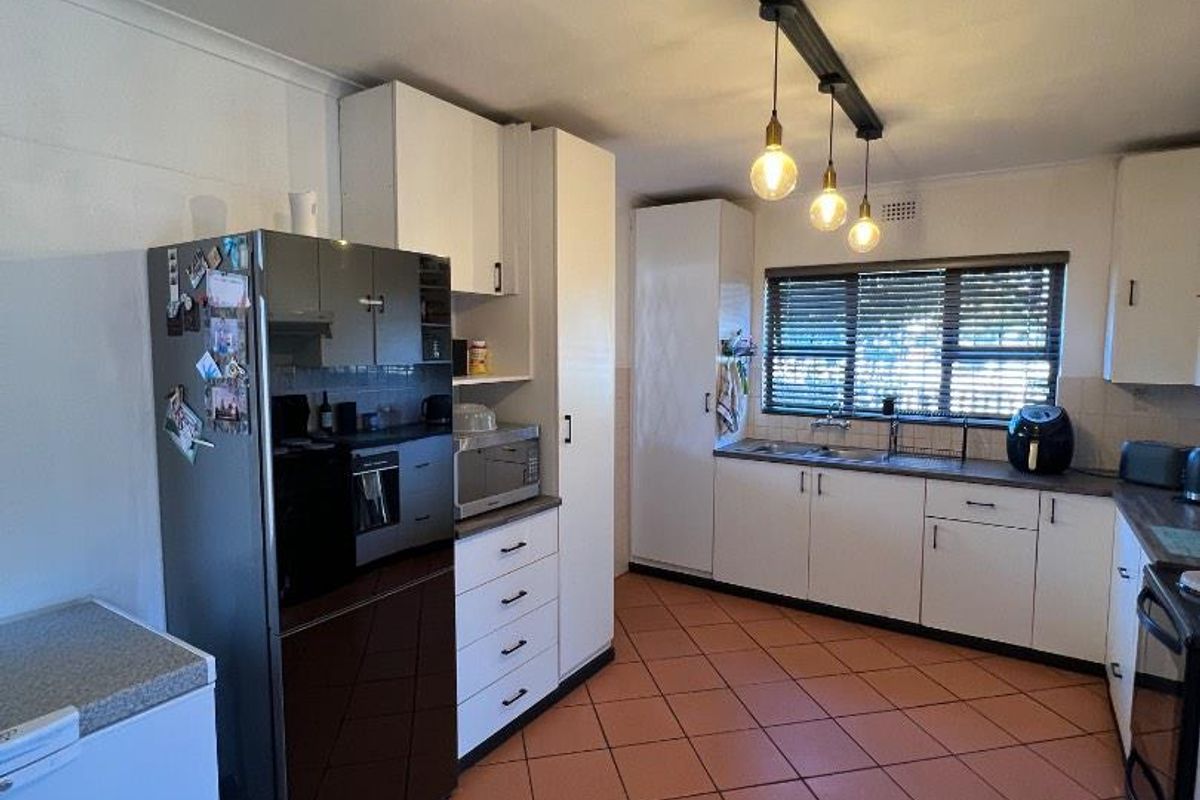 A functional kitchen featuring white cabinetry, tiled flooring, and modern pendant lighting, providing a practical workspace with ample storage and counter space.