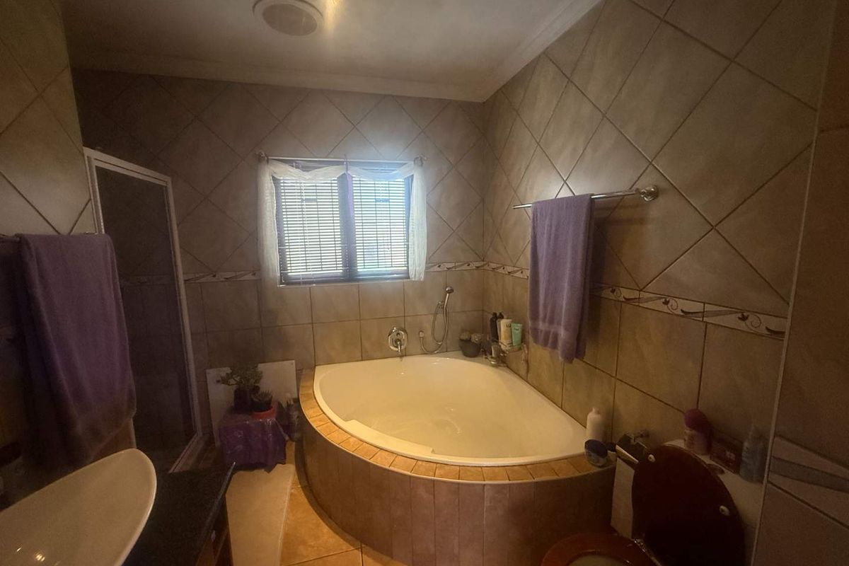 A functional bathroom featuring a corner bathtub, separate shower enclosure, and tiled finishes throughout, offering a practical layout for daily use.