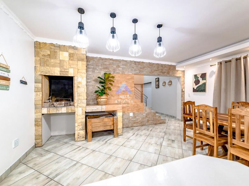 A well-maintained living area featuring a prominent stone-clad indoor braai, tiled flooring, and modern pendant lighting, creating a warm and inviting atmosphere.