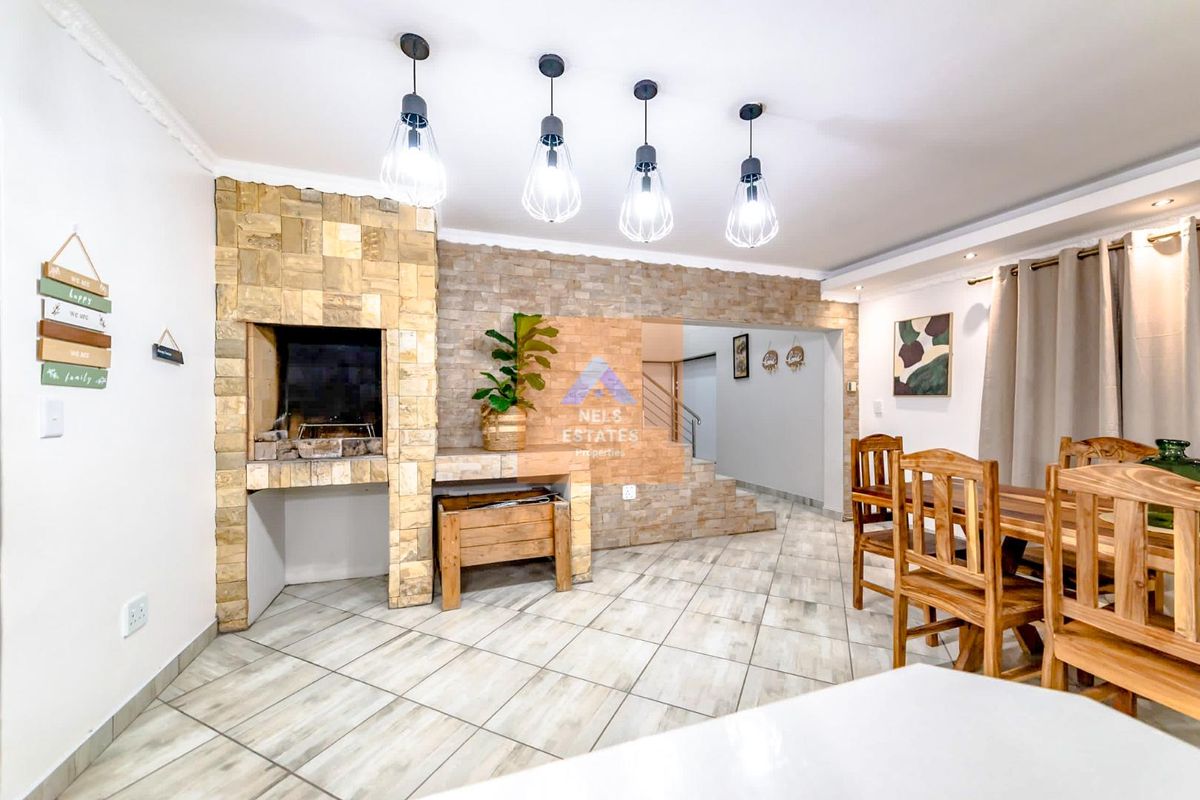 A well-maintained living area featuring a prominent stone-clad indoor braai, tiled flooring, and modern pendant lighting, creating a warm and inviting atmosphere.