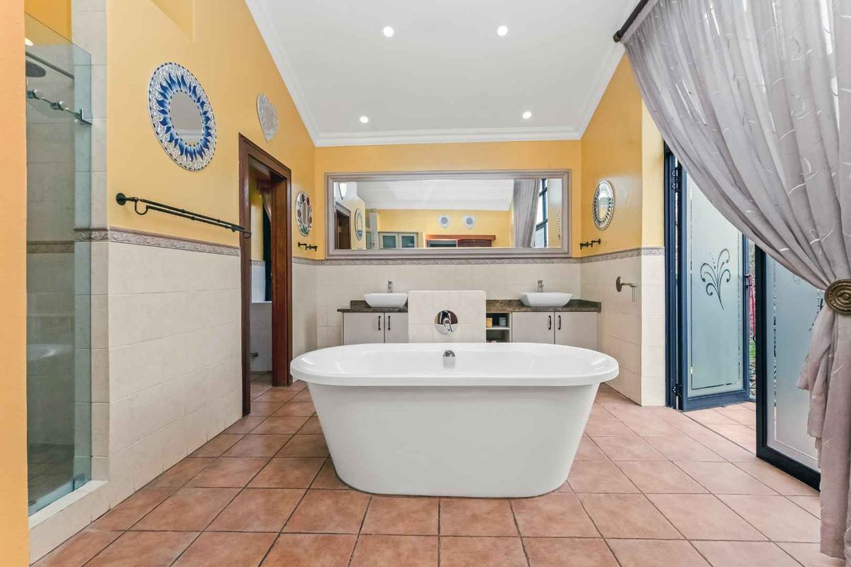Spacious bathroom featuring a central freestanding bathtub, dual vanity with stone countertop, glass-enclosed shower, and tiled flooring with direct outdoor access.