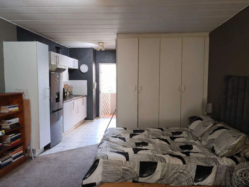 Open-plan studio layout featuring a compact kitchen area with built-in cabinetry and a bedroom section with integrated floor-to-ceiling cupboards.