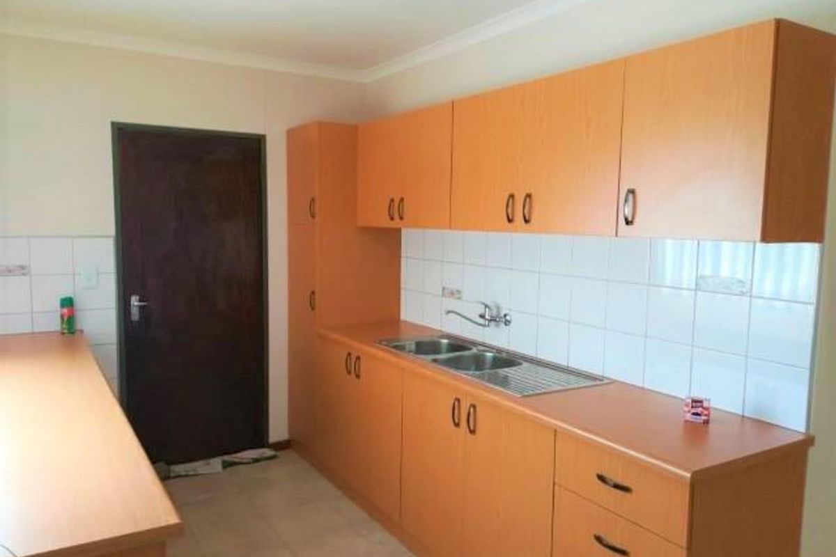 A functional kitchen featuring wood-look cabinetry, a double-basin stainless steel sink, and white tiled splashbacks, providing ample storage and workspace.