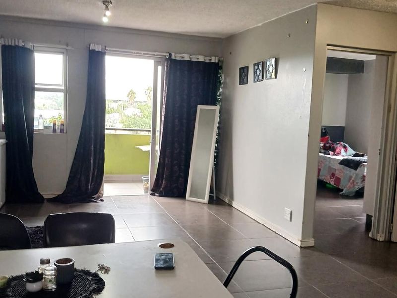 Open plan living area featuring tiled flooring and a sliding glass door leading to a balcony, with an adjacent view into a bedroom.