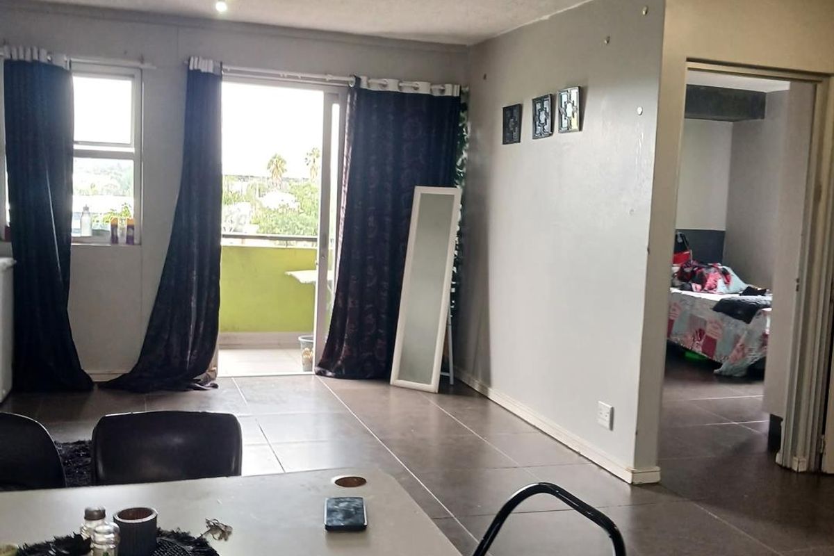 Open plan living area featuring tiled flooring and a sliding glass door leading to a balcony, with an adjacent view into a bedroom.