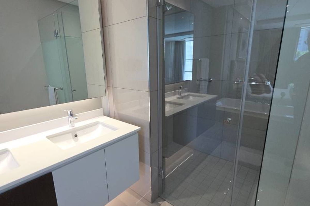 Modern bathroom featuring a double vanity with integrated sinks, large wall-mounted mirror, and a glass-enclosed walk-in shower with tiled finishes.