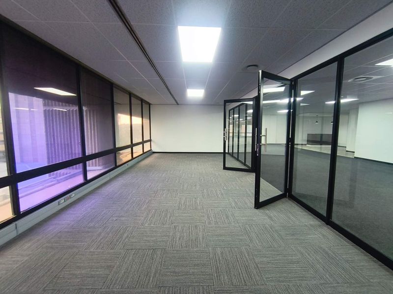 A modern, vacant office space featuring glass partitions, carpet tiles, and a suspended ceiling with recessed lighting, offering a clean and professional work environment.