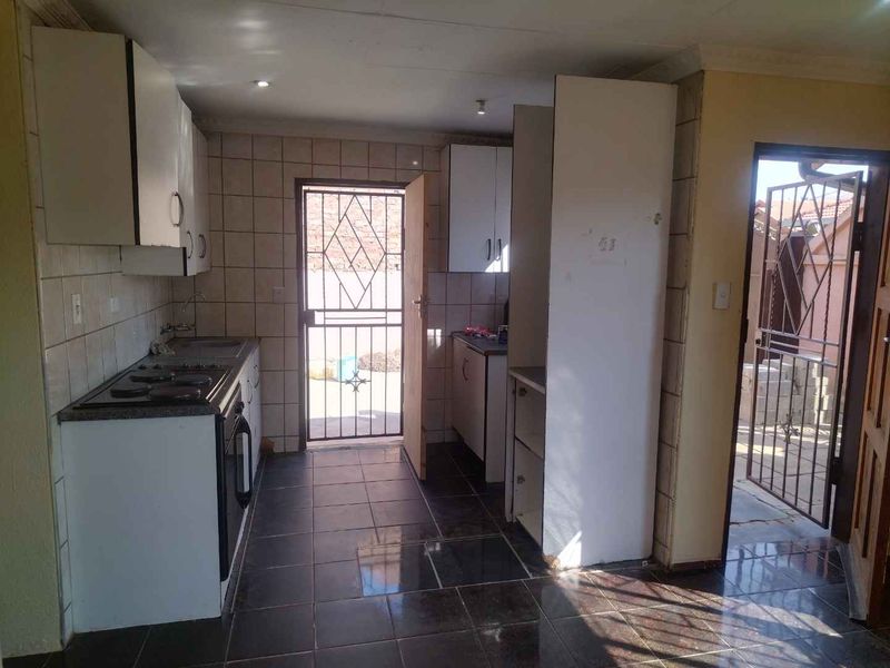A functional kitchen featuring tiled flooring, built-in cabinetry, and an electric stove, with direct access to the exterior via a security gate.