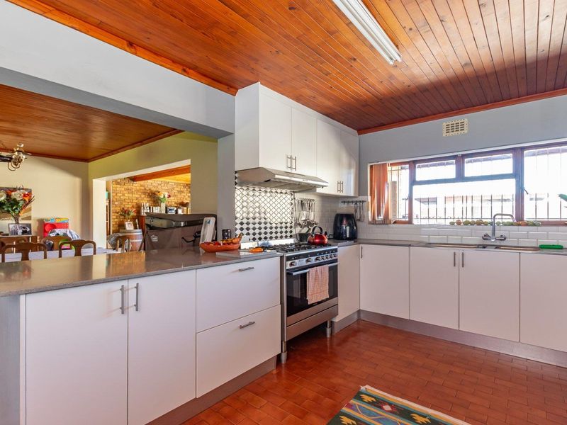 A functional kitchen featuring white cabinetry, a gas stove with extractor fan, tiled backsplash, and warm timber ceiling finishes.