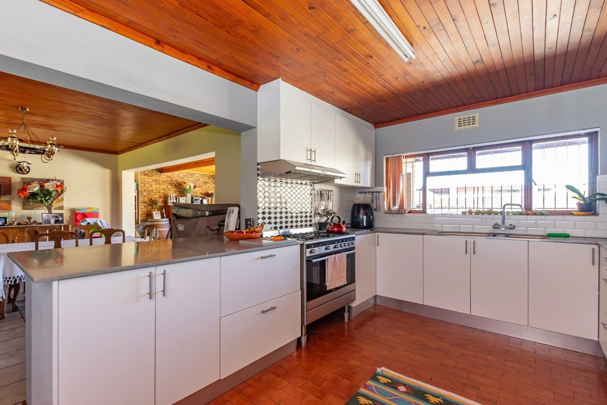 A functional kitchen featuring white cabinetry, a gas stove with extractor fan, tiled backsplash, and warm timber ceiling finishes.