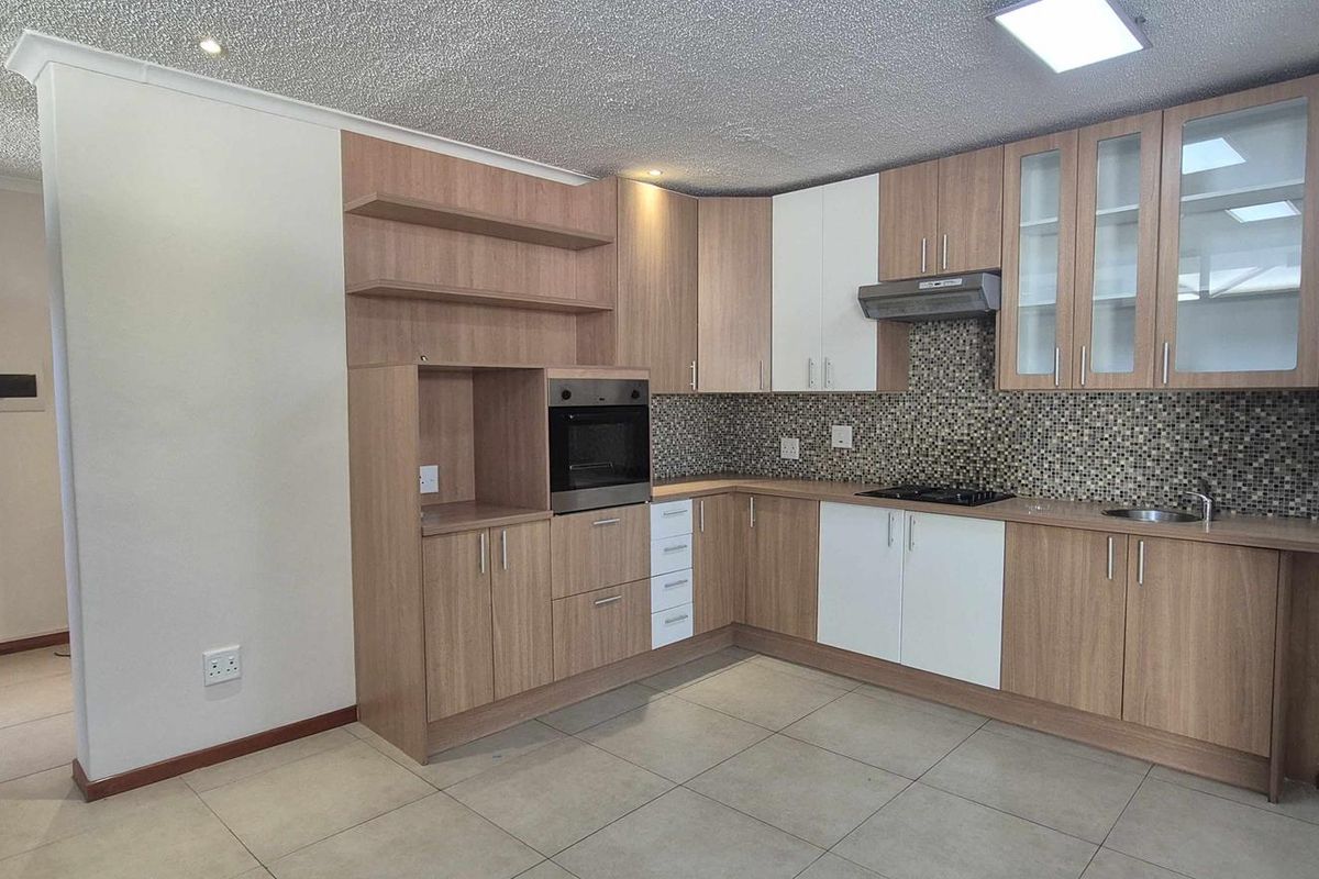 Modern kitchen featuring wood-tone and white cabinetry, built-in oven, gas hob, extractor fan, and mosaic tile backsplash with tiled flooring.