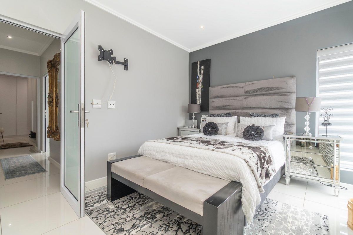 A well-maintained bedroom featuring tiled flooring, neutral grey walls, and a modern glass-panelled door leading to the hallway.