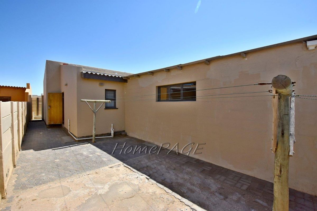 A rear exterior view of the property featuring paved ground, exterior walls, and a fixed washing line structure.