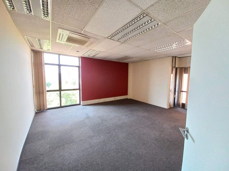 A vacant office space featuring a suspended ceiling with integrated lighting, air conditioning unit, large windows, and carpeted flooring.