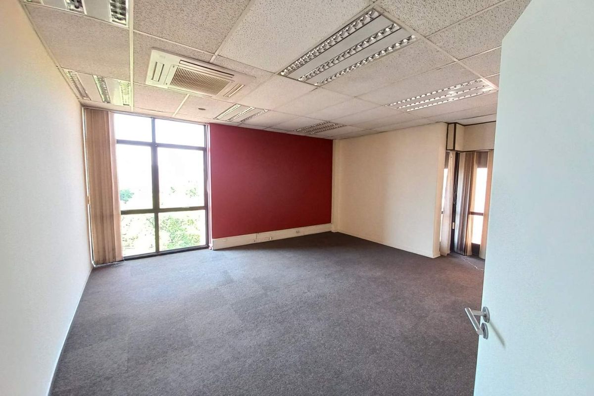 A vacant office space featuring a suspended ceiling with integrated lighting, air conditioning unit, large windows, and carpeted flooring.