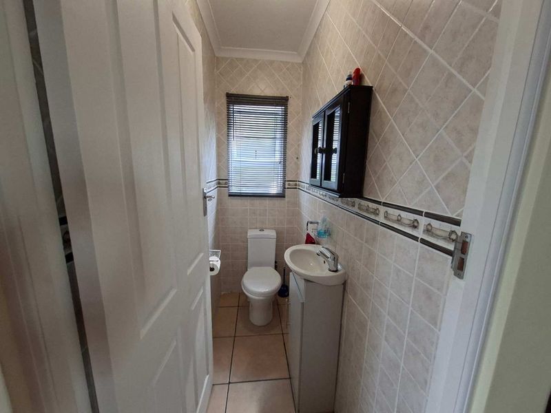 A compact guest bathroom featuring tiled walls and flooring, a pedestal basin, and a toilet.
