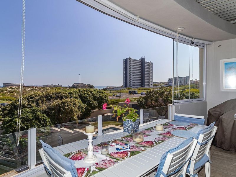 Covered balcony featuring a glass balustrade and retractable glass panels, offering expansive views of the surrounding landscape and coastal area.