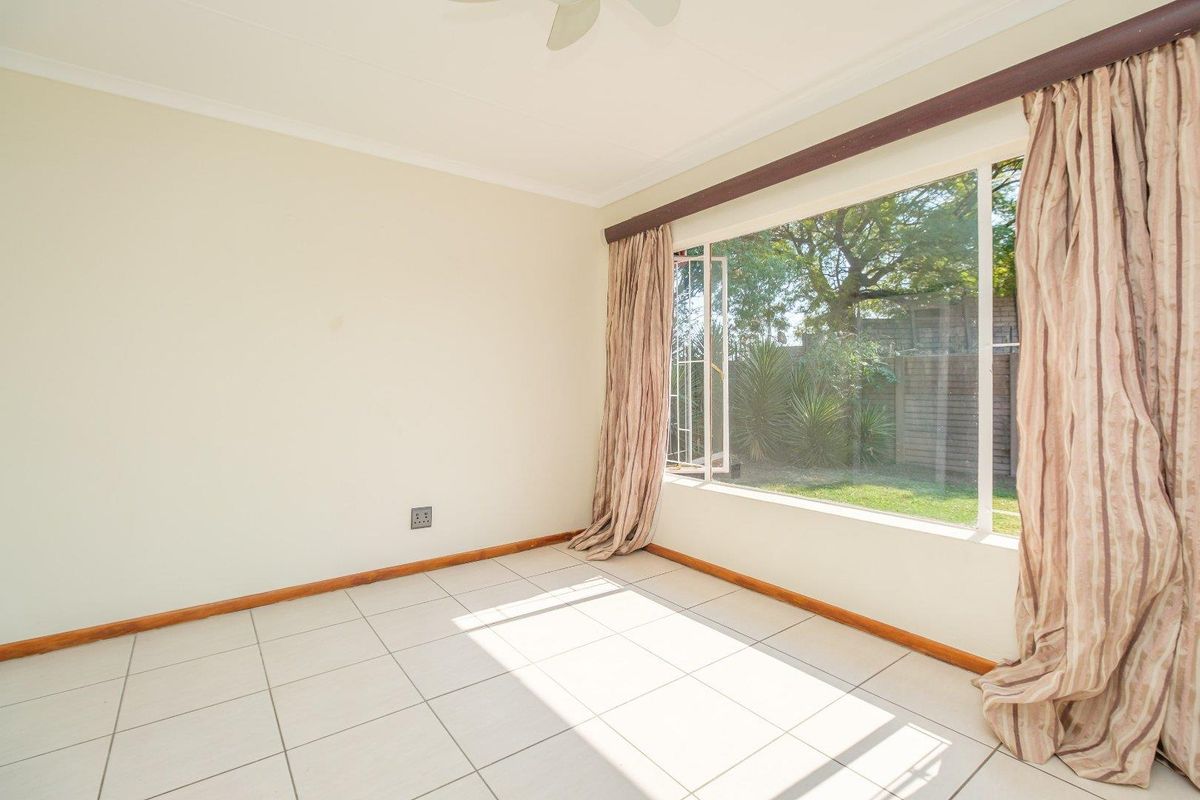 A bright, empty bedroom featuring tiled flooring, a ceiling fan, and a large window overlooking the garden.