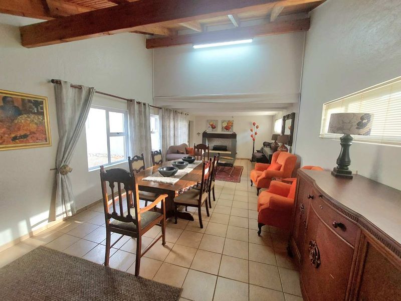 Spacious open-plan living and dining area featuring exposed timber ceiling beams, tiled flooring, and a built-in fireplace.