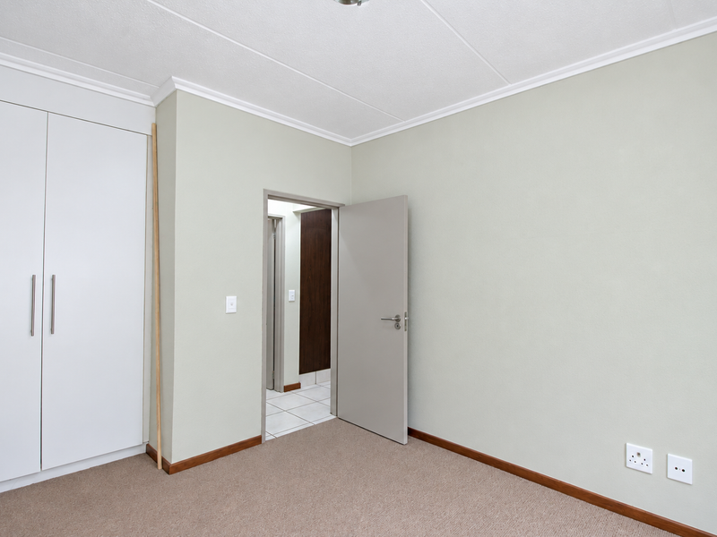 A clean, empty bedroom featuring neutral walls, carpeted flooring, and built-in cupboards, offering a versatile space ready for personalization.