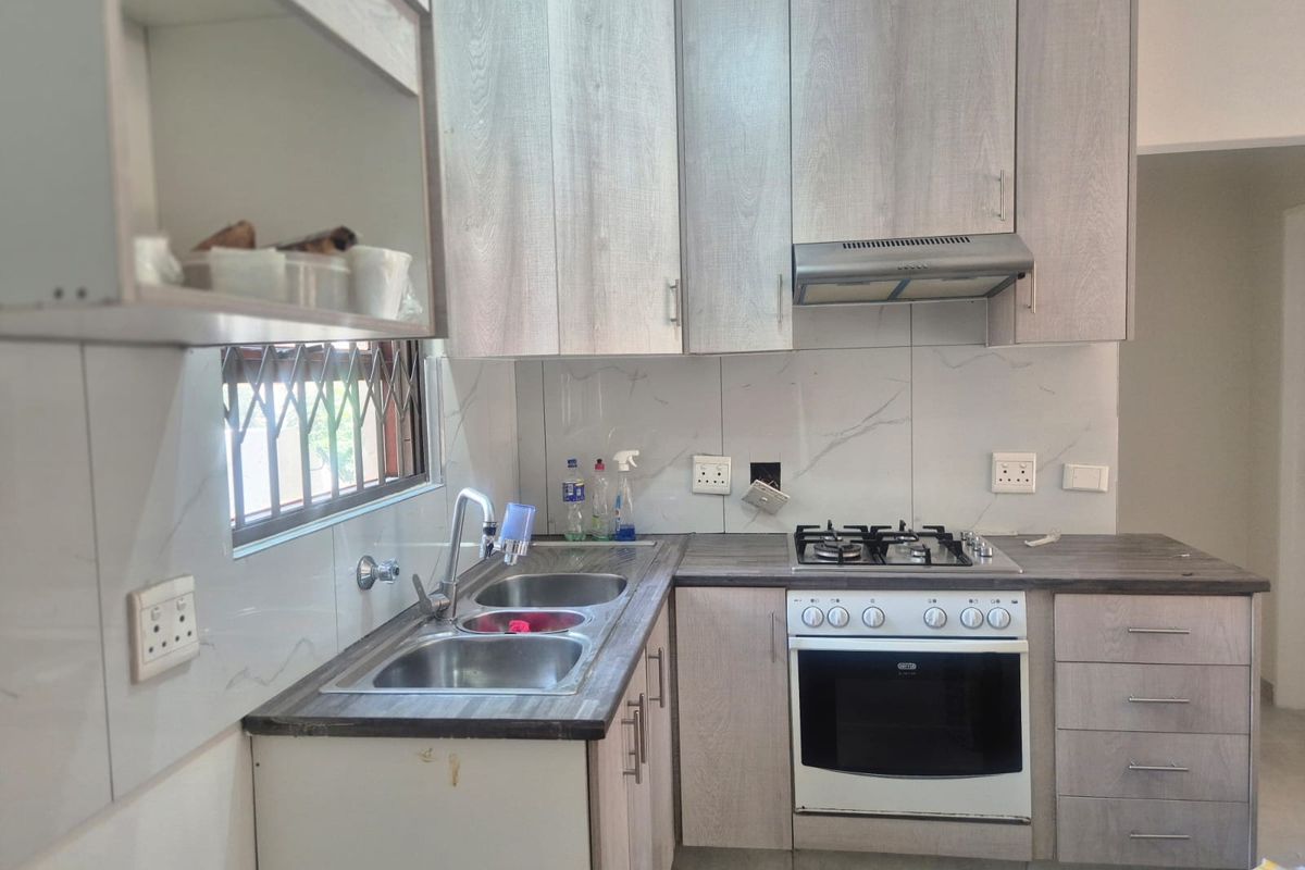 A functional kitchen featuring light wood-grain cabinetry, laminate countertops, a gas hob with oven, and a double bowl sink with tiled splashback.