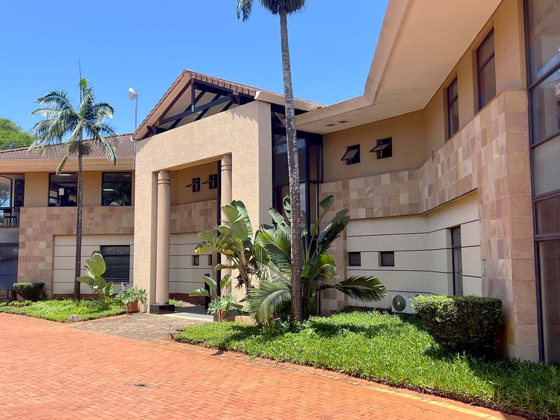 A well-maintained office building exterior featuring stone cladding, a covered entrance, and a spacious brick-paved driveway with landscaped garden areas.