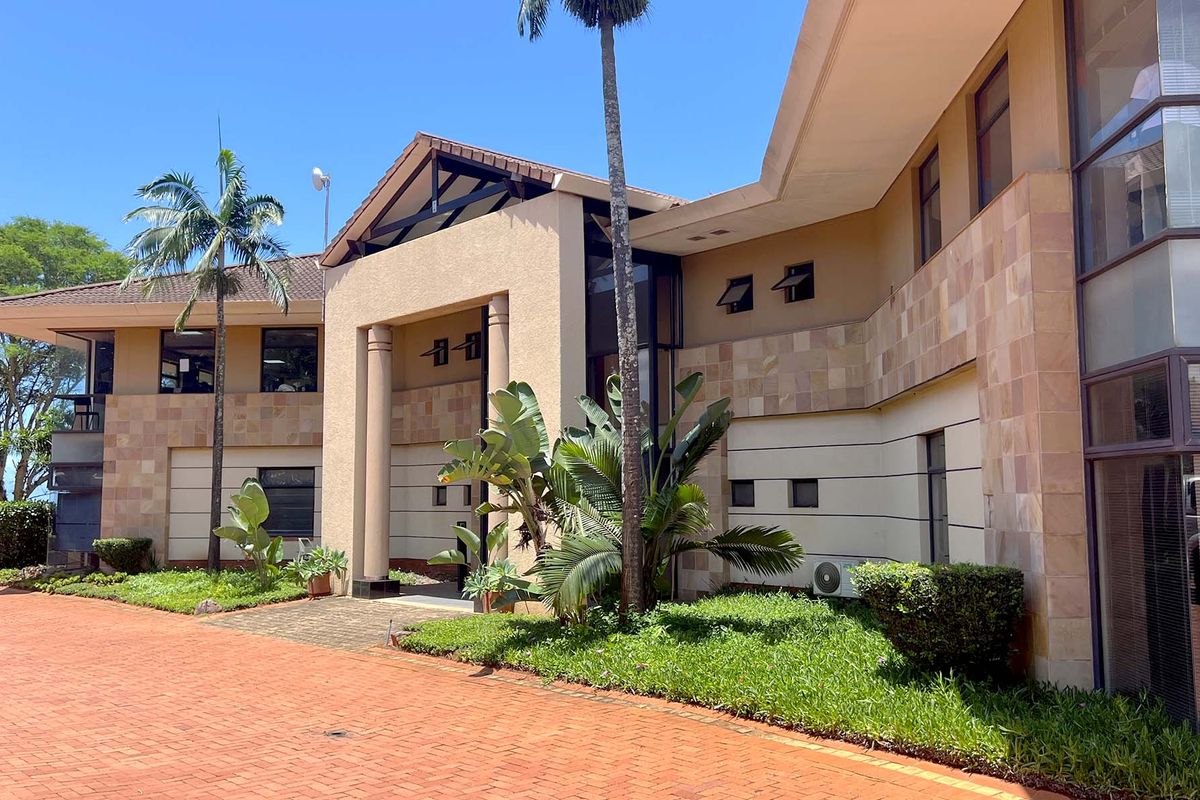 A well-maintained office building exterior featuring stone cladding, a covered entrance, and a spacious brick-paved driveway with landscaped garden areas.
