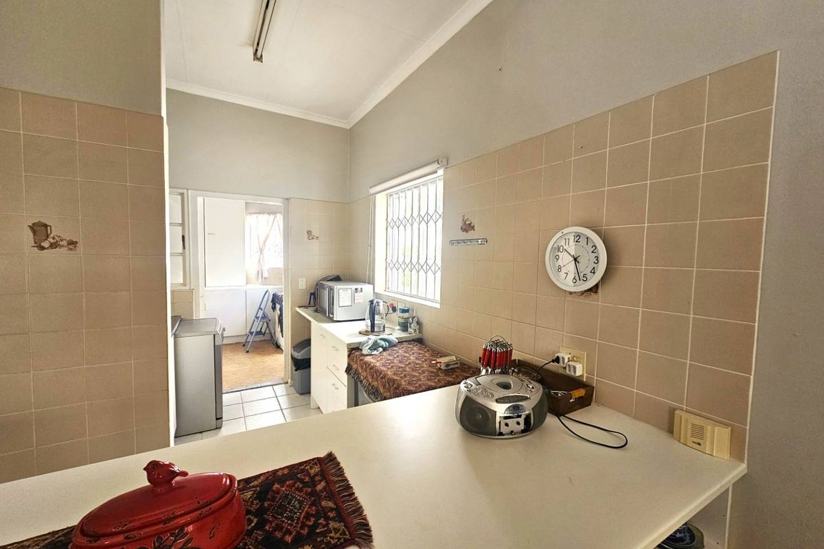 A functional kitchen area featuring tiled splashbacks, built-in cabinetry, and a breakfast bar, with an adjacent utility space visible through the doorway.