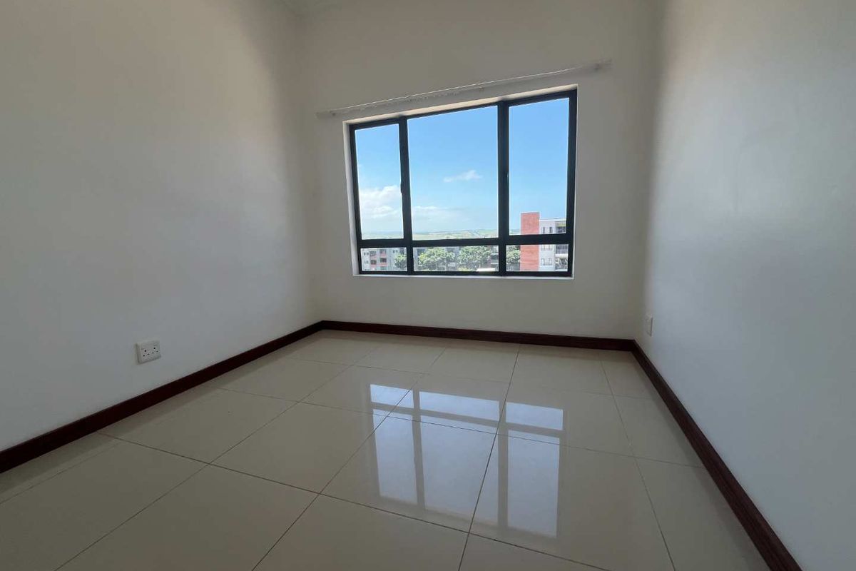 A bright, empty bedroom featuring large windows with a view, tiled flooring, and dark wood skirting boards.