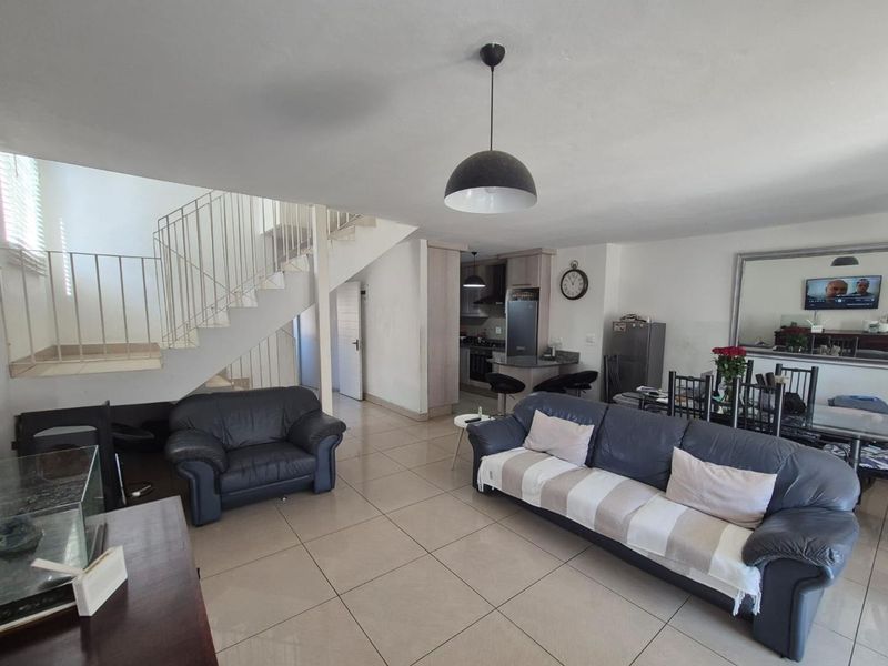 Open-plan living and dining area featuring tiled flooring, a central staircase with metal balustrade, and an integrated kitchen with breakfast counter.