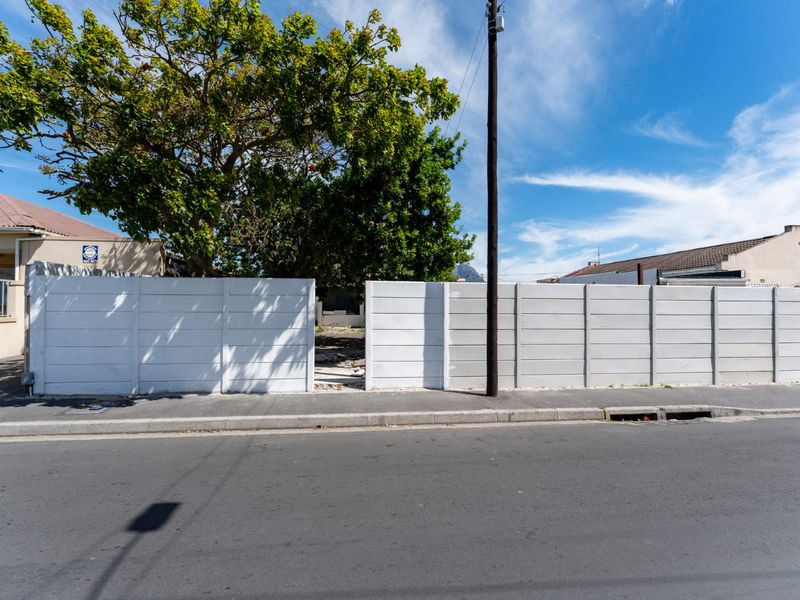 Street view of the property frontage featuring a precast concrete boundary wall with a central opening and adjacent asphalt road.